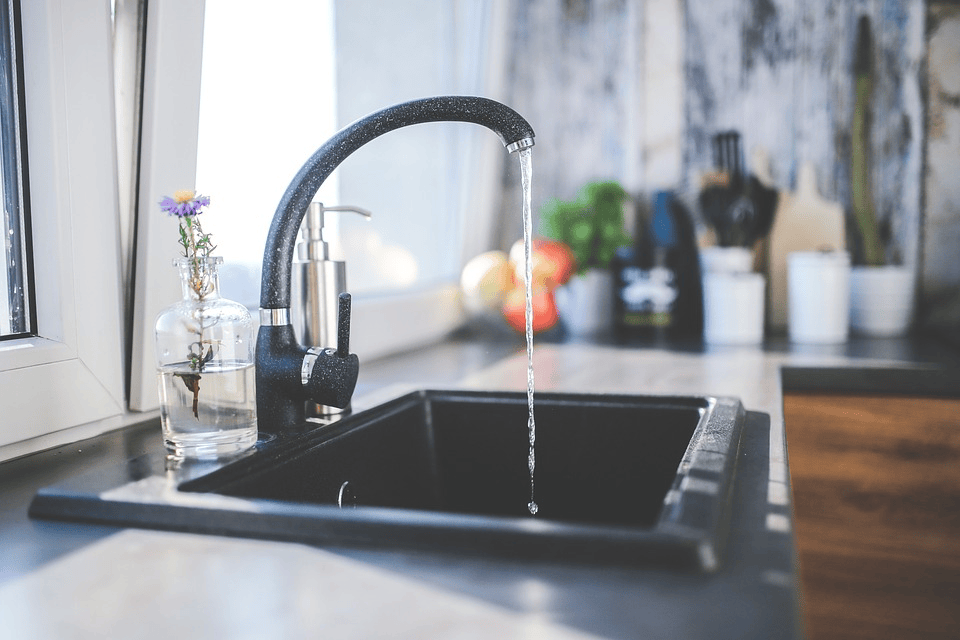 a gray kitchen sink decorated with a purple flower in a jar with the water running